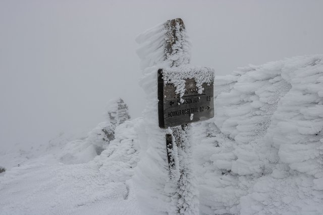 Rime‑encrusted signpost emerging from deep snow at Mount Madison’s summit.